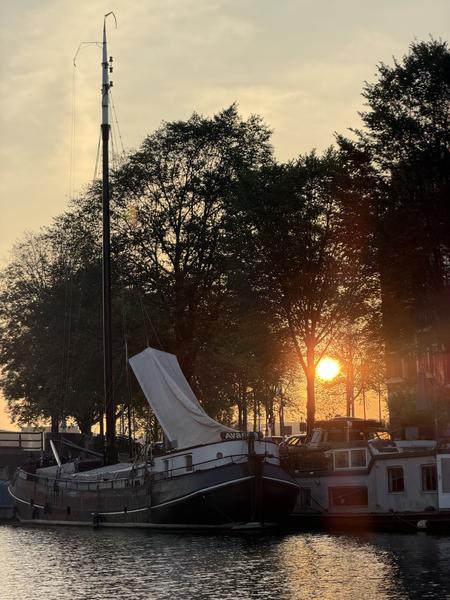 This tranquil photo captures a beautiful sunset over the Kalkmarkt in Centrum, Amsterdam, illuminating a sailboat and several houseboats docked along the canal
